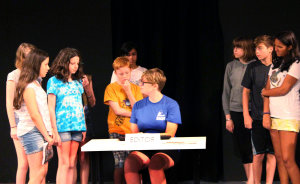 During dress rehearsal, Olympian campers investigate the Greenbelt News Review, with Anja Holland playing Mary Lou Williamson.