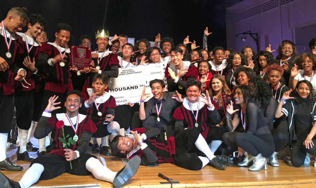 A crowd of smiling high school students, wearing red and black, gathers around a large presentation check.
