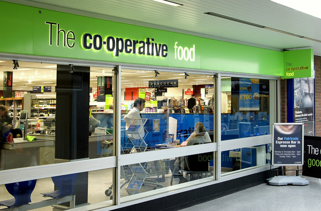 A UK grocery co-op is shown. The front wall consists of large glass windows below the green storefront sign of "The co-operative food"