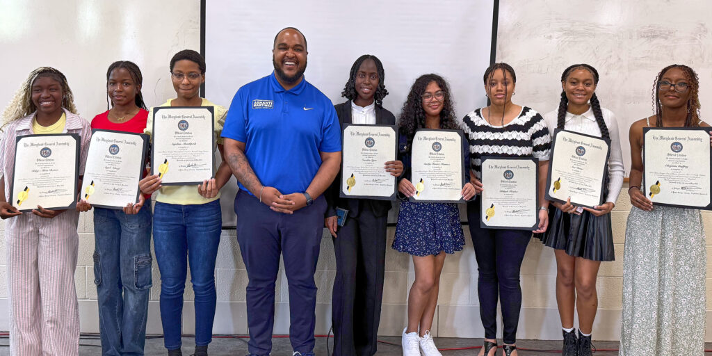 Maryland State Delegate Ashanti Martinez, wearing a blue shirt, stands amid a line of student winners who hold framed prize certificates.
