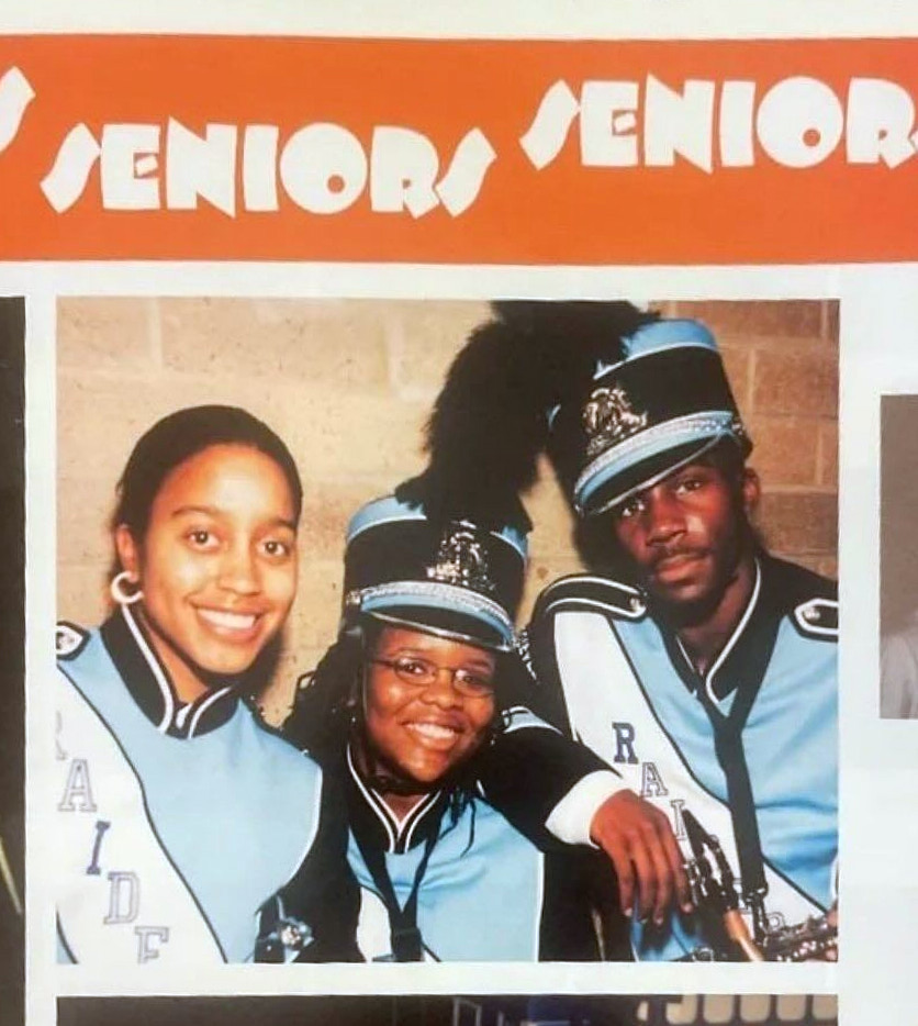 Below an orange banner with the words SENIORS SENIORS in white capital letters, is a photo of three brown-skinned students wearing band uniforms in light blue and black, with a white crossbody banner reading RAIDERS. The two students at right wear hats in black and light blue, with black feather tops.