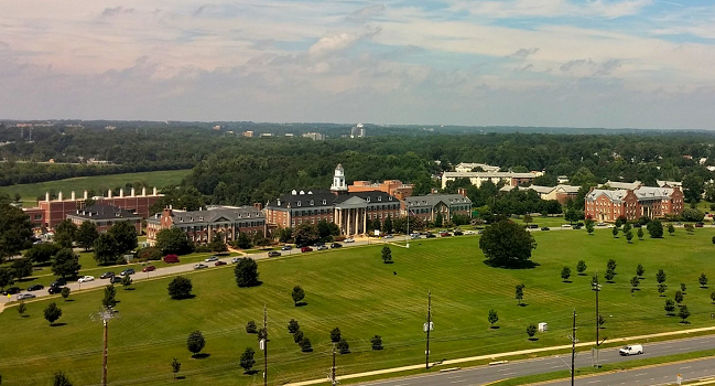 A low aerial shot of multiple buildings and a large field with trees.