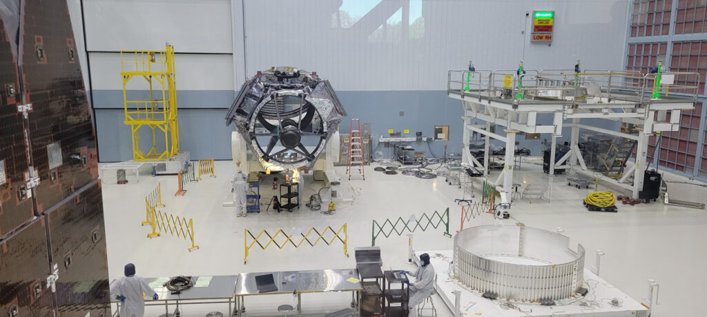 The gray hexagonal bulk of the telescope rests on a stand on a white floor. Equipment and shelves surround the edges of the room.