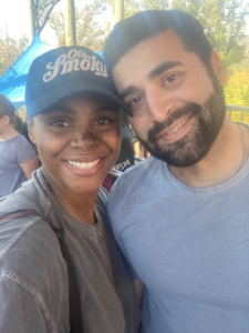 A smiling brown-skinned woman in a gray shirt and blue "Ole Smoky" baseball cap, and a smiling beige-skinned man with black hair, mustache, and beard, in a blue shirt.