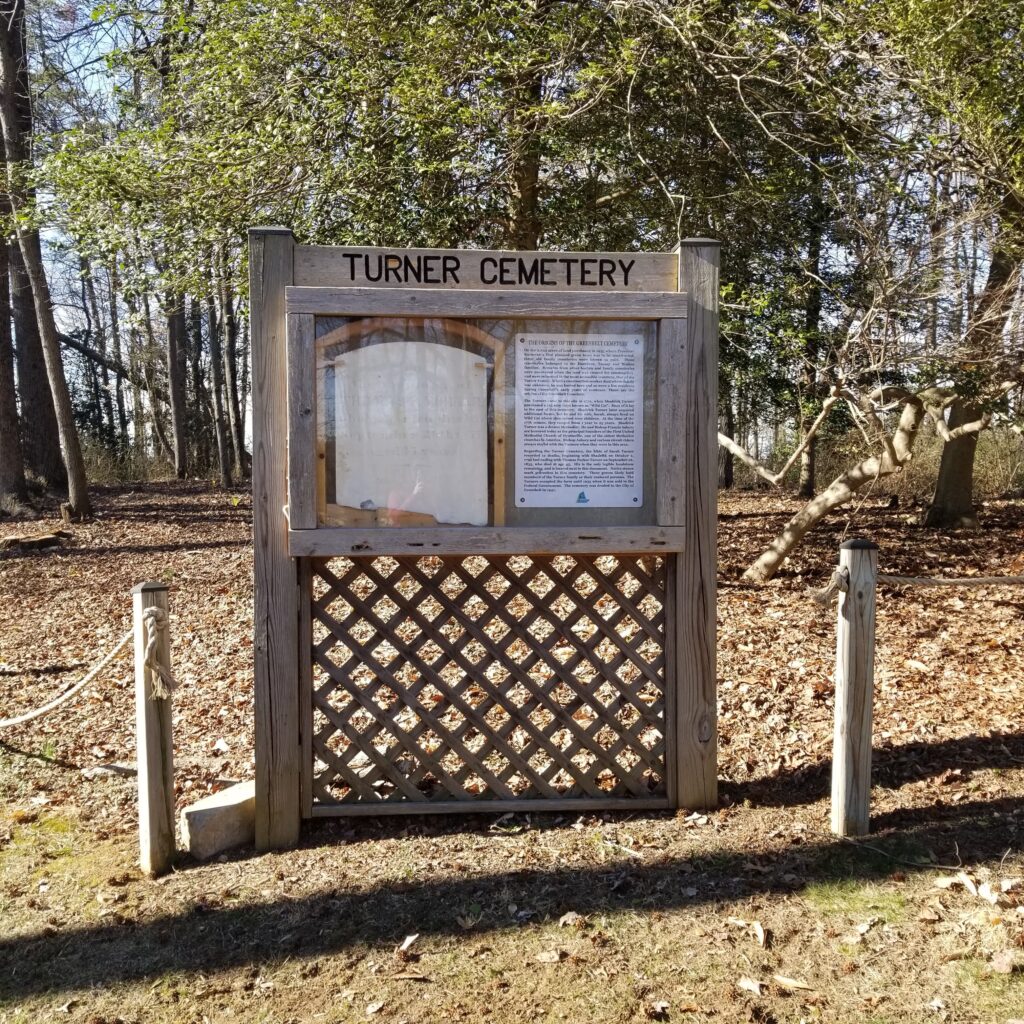 A glass-covered outdoor display case in a wooden frame, in an open field, with trees in the background.