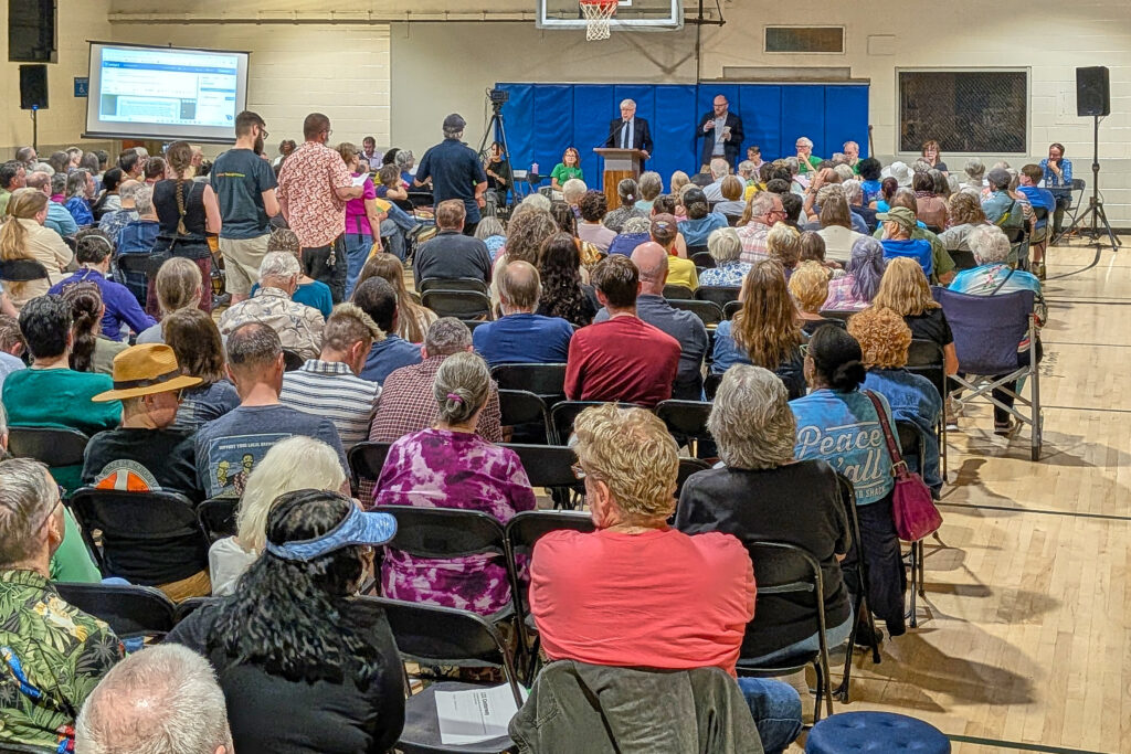 A gymnasium is filled with rows of chairs, with people sitting in all of them.